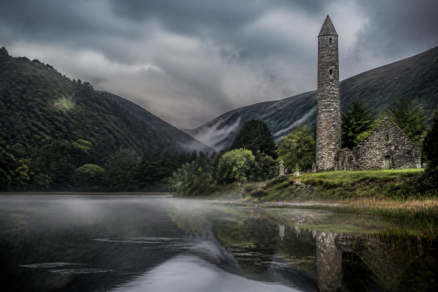The round tower and monastic ruins at Glendalough reflected in a still, misted lake