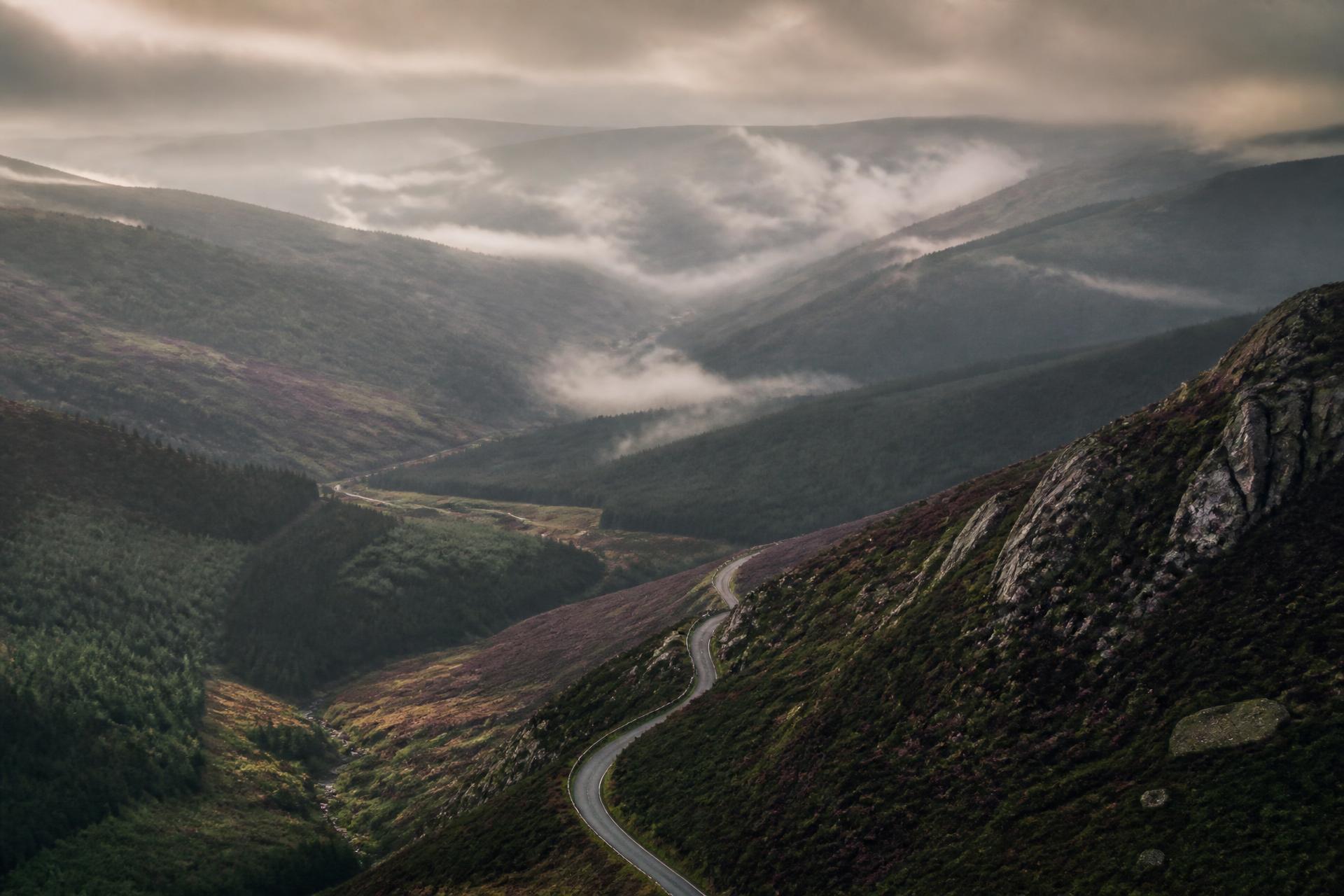 Mist rolling through the Wicklow mountains at dawn with a single road winding through the valley